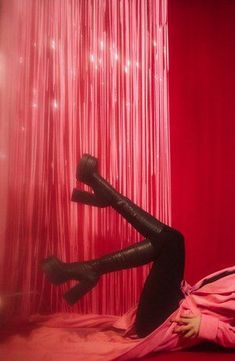 a woman laying on top of a bed in front of a red curtain with her legs up