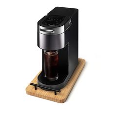 a black coffee maker sitting on top of a wooden tray with a drink in it