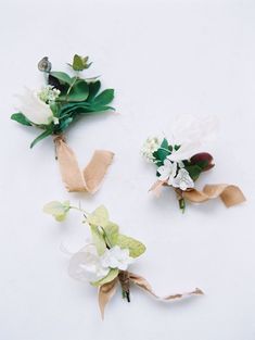 three boutonniers with white flowers and green leaves