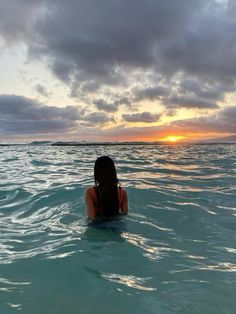 a woman is sitting in the ocean watching the sun go down over the water with her back turned to the camera