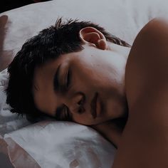 a young man sleeping on top of a bed with his eyes closed and head turned to the side