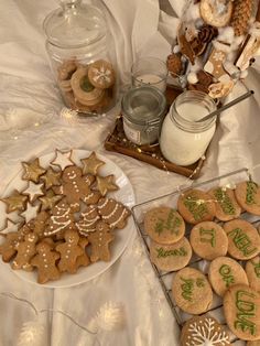 cookies and other holiday treats are arranged on a white tablecloth with glass jars filled with snowflakes