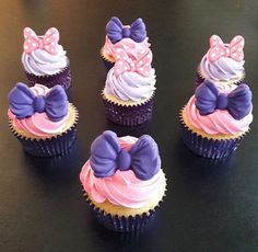 six cupcakes with pink, purple and white frosting on them sitting on a table