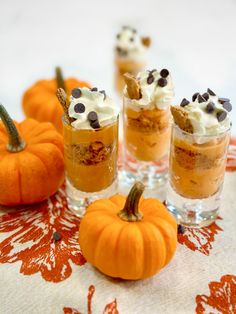 mini pumpkin desserts with chocolate chips and whipped cream in them on a tablecloth