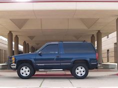 a blue suv is parked in front of a parking garage with columns on either side