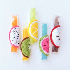 crocheted fruit and vegetable lollipops are lined up on a white surface