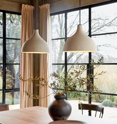 two lamps hanging over a wooden table in front of large windows