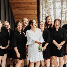 a group of women standing next to each other in front of a wooden wall and trees