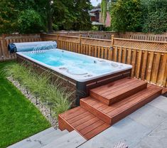 a hot tub in the middle of a backyard with steps leading up to it and a wooden fence behind it