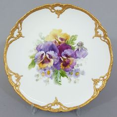 a plate with flowers painted on the side and gold trimmings around the edge