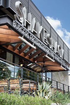 the outside of a restaurant with wooden benches and plants in front on a sunny day