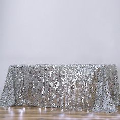 a silver sequin table cloth on top of a wooden floor in front of a white wall