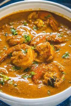 a white bowl filled with shrimp and tomato soup on top of a blue table cloth