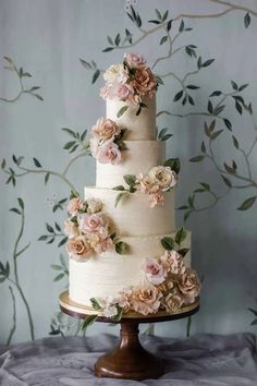 a three tiered wedding cake with pink flowers on the top and bottom, sitting on a wooden stand