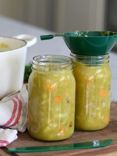 two jars filled with pickles sitting on top of a cutting board next to a bowl