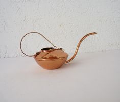 a small copper teapot with a handle on a white table next to a wall