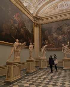 a woman is standing in front of some statues and paintings on the wall behind her