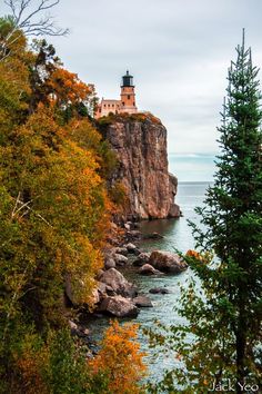 a lighthouse on top of a cliff next to the ocean with trees in front of it