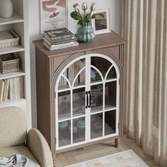 a living room with a book shelf, chair and vase filled with flowers on top of it