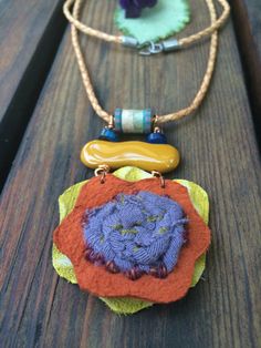 "This is an original Zasra design. This necklace is a one of a kind, handmade, eco conscience, artisan leather fiber flower necklace. For this necklace I have handmade the focal pendant, first by making the recycled jersey flower center, which I hand stitched, and then layered onto recycled leather. I then wire wrapped onto a beautiful stone double drilled moukaite stone bead, and electric blue dyed stone beads. I completed with a hand painted wooden barrel bead, and strung from a tan woven brai Bohemian Brown Flower Necklace, Fiber Necklace, Funky Necklace, Textile Necklace, Eco Jewelry, Eco Clothing, Necklace Leather, Wooden Barrel, Necklace Flower