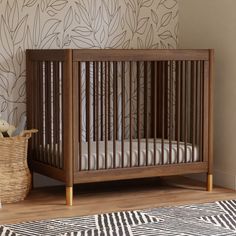 a baby crib in front of a wall with leaves on it and a basket next to it