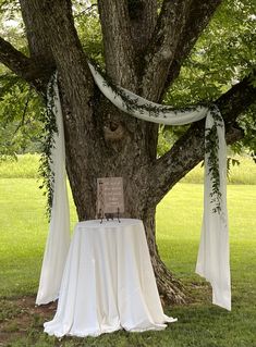 a tree with a white cloth draped over it and a sign on the table under it