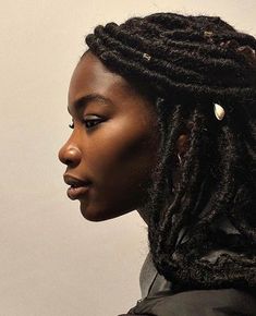 a woman with dreadlocks looking off to the side in front of a white wall