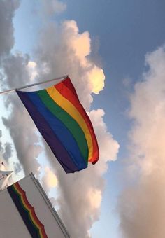 a rainbow flag flying high in the sky on a cloudy day with clouds behind it