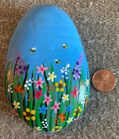 a painted rock with flowers and bees on it next to a penny