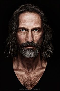 a man with long hair and beard wearing a black shirt is looking at the camera