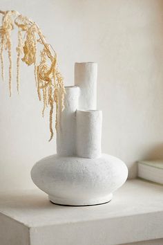 two white vases sitting on top of a shelf next to a book and plant