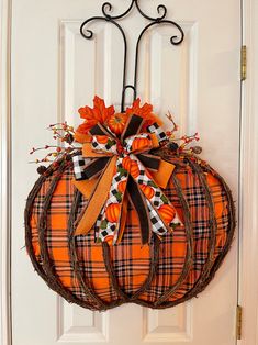 an orange and black plaid pumpkin wreath hanging on a white door with a wrought iron hanger