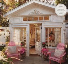 a small white house with pink chairs and potted flowers on the front porch area