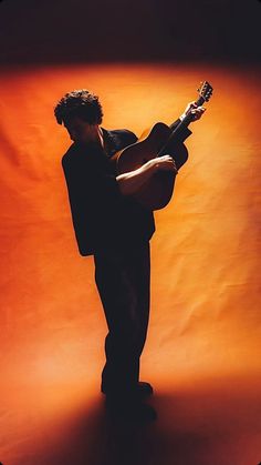 a man standing in front of an orange background holding a guitar