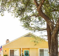 a yellow house with an american flag on the front door and trees in front of it