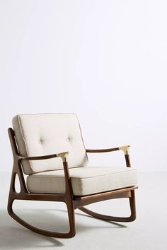 a rocking chair with beige upholstered fabric and wooden frame, in front of a white wall