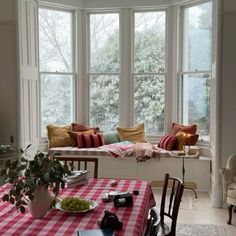 a dining room table with red and white checkered cloth on it, next to a bay window