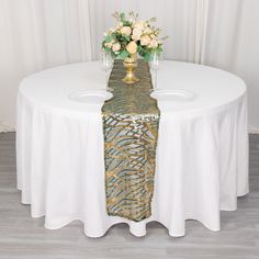 a white table topped with two vases filled with flowers and greenery on top of it