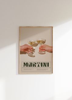 two hands holding wine glasses in front of a white wall with the word martini on it