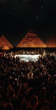 a large group of people standing in front of pyramids at night with their hands up