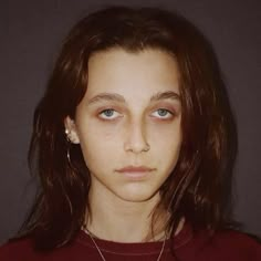 a young woman with blue eyes and long hair wearing a red shirt is looking at the camera