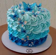 a blue cake with butterflies on it sitting on top of a white plate and brown table