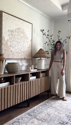 a woman standing in front of a large painting on the wall next to a dresser