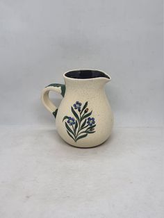 a white pitcher with blue flowers painted on the front and bottom, sitting on a table