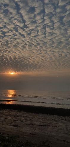 the sun is setting over the ocean with clouds in the sky and water on the beach