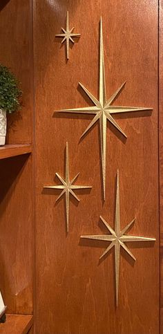 three metal stars on a wood paneled wall next to a book shelf and plant