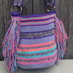 a crocheted purse with tassels hanging from it's side on a wooden surface