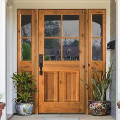 a wooden door with two planters on the front porch and sidelights above it