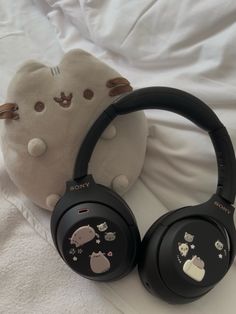 two black headphones sitting on top of a white bed next to a stuffed animal