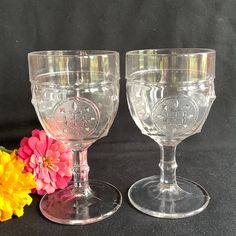 two clear goblets sitting next to each other on a black surface with flowers